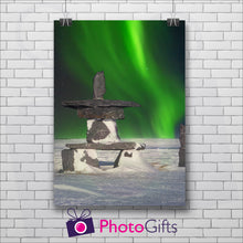 Load image into Gallery viewer, White painted brick wall with a portrait picture hanging by two metal clips. The picture is of a snowy land with a stone sculpture with some snow on and in the night sky behind is the Northern Lights showing in vivid green. Picture as produced by Photogifts.co.uk