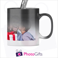 Load image into Gallery viewer, Personalised 10oz black colour change mug with your own choice of image shown in the stage where half the mug has received hot liquid and is in the process of revealing the image. As produced by Photogifts.co.uk
