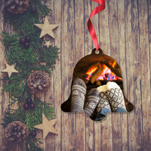 Load image into Gallery viewer, Dark wooden background with a Christmas Garland stretched out on the Left hand side from top to bottom. On the garland are some wooden strs and fir cones along with some dark red berries. To the right of the garland is a Christmas Bell Decoration with a red ribbon. On the bell is a picture of two peoples socked feet infant of an open log fire. Bell Decoration as supplied by Photogifts.co.uk
