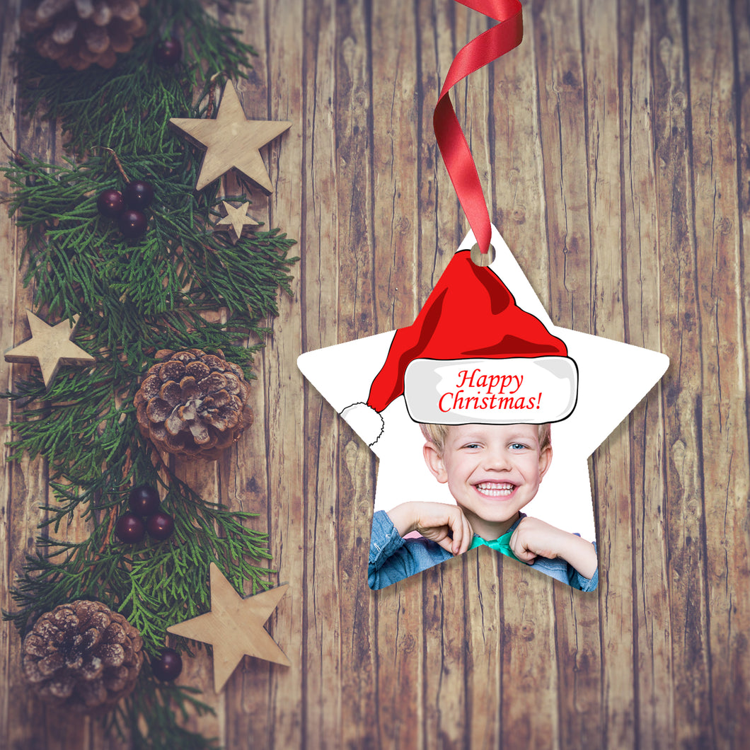 Dark wooden background with a Christmas Garland stretched out on the Left hand side from top to bottom. On the garland are some wooden stars and fir cones along with some dark red berries. To the right of the garland is a Christmas Decoration in the shape of a star with a red ribbon. The decoration is a picture of a boy's head and shoulders with a santa hat saying Merry Christmas. Decoration as supplied by Photogifts.co.uk