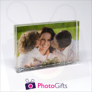 152mm x 102mm (6" x 4") clear acrylic freestanding block, in landscape orientation,  that can be personalised with your own choice of image. The block is filled with tiny silver glitter suspended within a clear liquid. The chosen image is clipped to the back of the block and shows through so you can see it behind the liquid. When the block is shaken the silver glitter will slowly make its way down to the bottom of the block similar to a snow globe