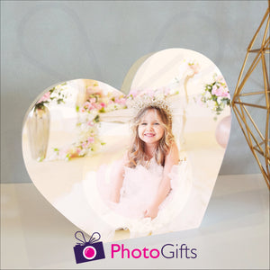 White wooden heart shaped block with a picture of a girl in a tiara and white dress sitting surrounded by flowers. White block and personalised photo as supplied by Photogifts.co.uk