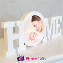 Load image into Gallery viewer, "Home" in a white painted wooden block with a picture of a mother and baby having fun stuck in the middle of the "O" of the home word. Shown on a white shelf as supplied by Photogifts.co.uk