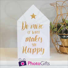 Load image into Gallery viewer, White wooden block in the shape of a house with the slogan "Do more of what makes you happy" printed on the front. The block is resting on a white shelf with a potted plant to one side. Personalised block as supplied by Photogifts.co.uk