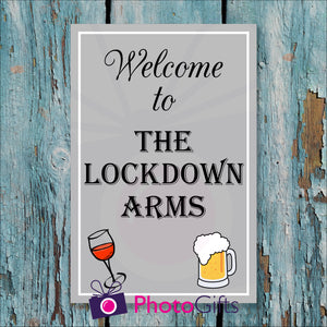 Light blue but worn painted wooden fence with a panel attached to the fence. On the panel is the wording "Welcome to The Lockdown Arms" and a picture of a wine glass and beer tankard. As produced by Photogifts.co.uk