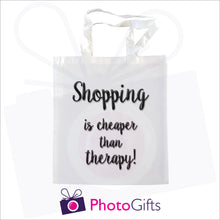 Load image into Gallery viewer, White tote shopping bag with the text "Shopping is cheaper than therapy!" printed in black on the bag