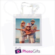 Load image into Gallery viewer, White tote shopping bag with a picture of a family in hat and sunglasses next to the sea on the bag