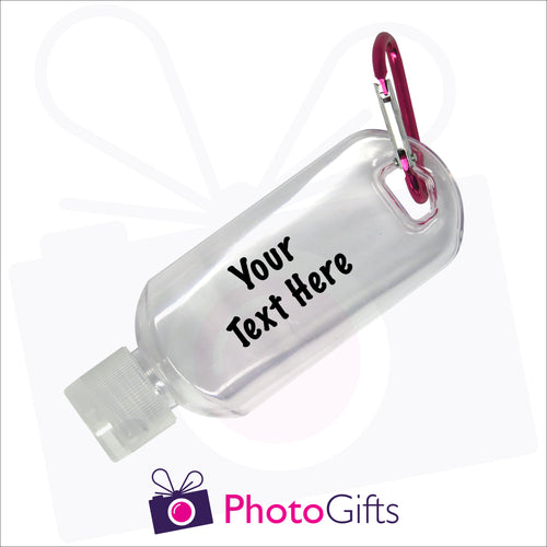 Close up image of a small 50ml clear plastic travel bottle together with a pink carabiner. Bottle is personalised with 