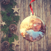 Load image into Gallery viewer, Dark wooden background with a Christmas Garland stretched out on the Left hand side from top to bottom. On the garland are some wooden stars and fir cones along with some dark red berries. To the right of the garland is a Christmas Decoration in the shape of a ball with a red ribbon. The decoration is a picture of the face of a woman in a white knitted beanie who is holding some snow in her open hands and is blowing some of the snow away. Decoration as supplied by Photogifts.co.uk
