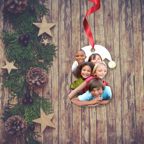 Dark wooden background with a Christmas Garland stretched out on the Left hand side from top to bottom. On the garland are some wooden stars and fir cones along with some dark red berries. To the right of the garland is a Christmas Decoration in the shape of a Snowman with a red ribbon. The decoration is printed with a picture of a group of kids piled on top of each other smiling at the camera. Decoration as supplied by Photogifts.co.uk