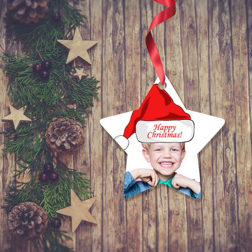 Dark wooden background with a Christmas Garland stretched out on the Left hand side from top to bottom. On the garland are some wooden stars and fir cones along with some dark red berries. To the right of the garland is a Christmas Decoration in the shape of a star with a red ribbon. The decoration is a picture of a boy's head and shoulders with a santa hat saying Merry Christmas. Decoration as supplied by Photogifts.co.uk