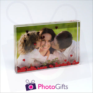 152mm x 102mm (6" x 4") clear acrylic freestanding block, in landscape orientation,  that can be personalised with your own choice of image. The block is filled with tiny red hearts suspended within a clear liquid. The chosen image is clipped to the back of the block and shows through so you can see it behind the liquid. When the block is shaken the red hearts will slowly make its way down to the bottom of the block similar to a snow globe