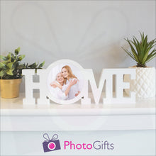 Load image into Gallery viewer, &quot;Home&quot; in a white painted wooden block with a picture of a mother and daughter having fun in stuck in the middle of the &quot;O&quot; of the home word. Shown on a white shelf with a couple of potted plants either side. Wooden word &quot;Home&quot; and personalised photo as supplied by Photogifts.co.uk
