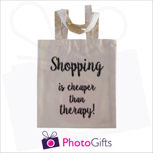 Natural coloured tote shopping bag with the text "Shopping is cheaper than therapy!" printed in black on the bag
