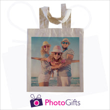Load image into Gallery viewer, Natural coloured tote shopping bag with a picture of a family in hat and sunglasses next to the sea on the bag
