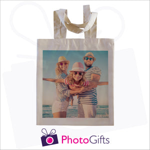 Natural coloured tote shopping bag with a picture of a family in hat and sunglasses next to the sea on the bag