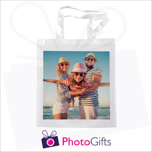 White tote shopping bag with a picture of a family in hat and sunglasses next to the sea on the bag
